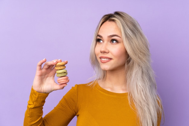 Ragazza dell'adolescente sopra i macarons francesi variopinti della tenuta porpora e cercare mentre sorridendo