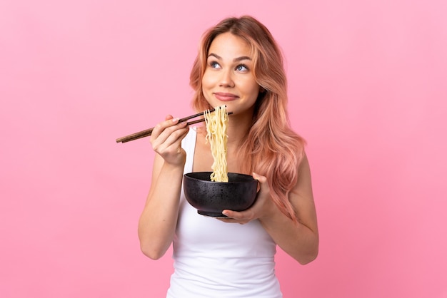 Ragazza dell'adolescente sopra il colore rosa isolato che tiene una ciotola di tagliatelle con le bacchette