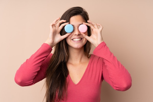 Ragazza dell'adolescente sopra la parete isolata che indossa i macarons francesi variopinti come vetri