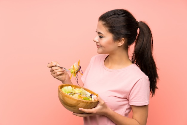 Ragazza dell'adolescente sopra la parete rosa isolata con insalata