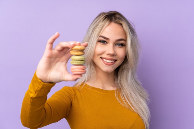 Ragazza dell'adolescente sopra la porpora isolata che tiene i macarons francesi variopinti e con l'espressione felice