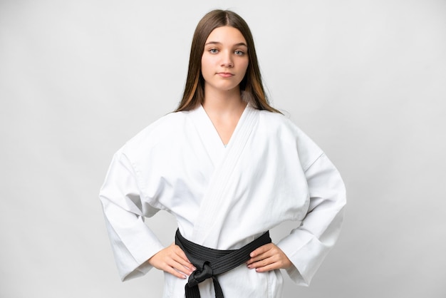 Ragazza dell'adolescente su sfondo bianco isolato facendo karate in posa con le braccia all'anca e sorridente