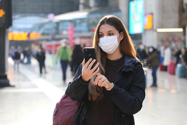 Ragazza dell'allievo che indossa la maschera protettiva che acquista il biglietto online con lo smartphone