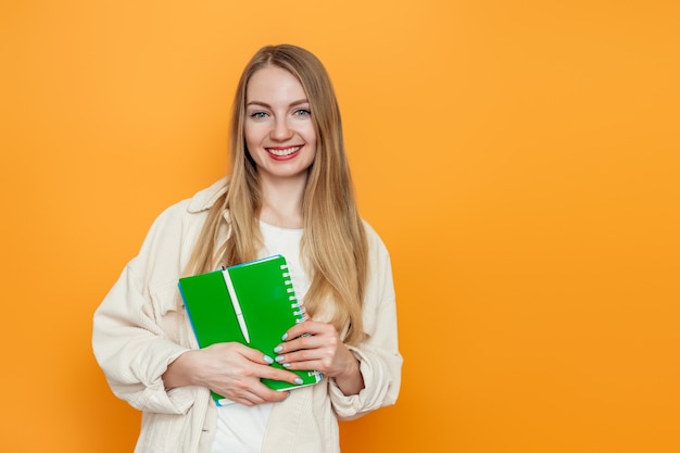 ragazza dell'allievo che tiene un libro, taccuino che sorride ed esamina la macchina fotografica