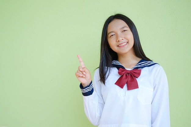 Ragazza dell'allievo del ritratto nella scuola dell'uniforme sulla parete verde. Ragazza asiatica adolescente