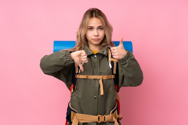 Ragazza dell'alpinista dell'adolescente con un grande zaino isolato sul segno buono-cattivo di fabbricazione rosa. Indeciso tra sì o no