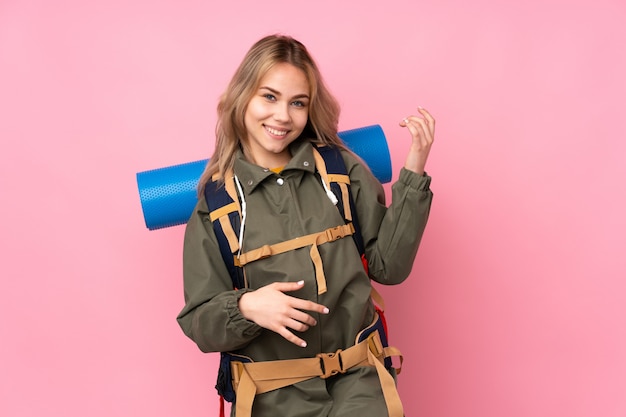 Ragazza dell'alpinista dell'adolescente con un grande zaino sulla parete rosa che fa gesto della chitarra