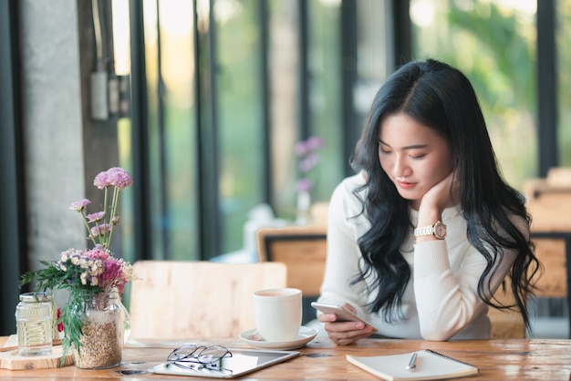 Ragazza dell&#39;Asia che utilizza telefono cellulare al caffè