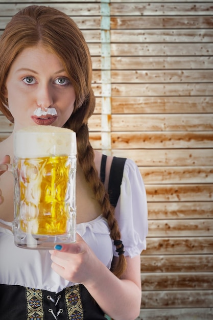 Ragazza dell'Oktoberfest che beve brocca di birra su sfondo di legno in legno chiaro