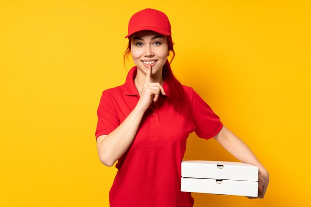 Ragazza della consegna della pizza che tiene una pizza sopra la parete isolata che mostra un segno del gesto di silenzio che mette il dito in bocca