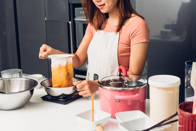 Ragazza della donna in cucina che cucina versando il tè tailandese caldo del gocciolamento