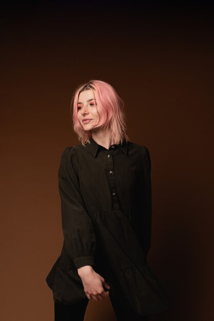 Ragazza della giovane donna con capelli rosa al ritratto dello studio del fondo della parete marrone