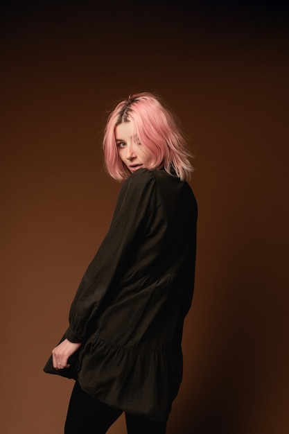 Ragazza della giovane donna con capelli rosa al ritratto dello studio del fondo della parete marrone