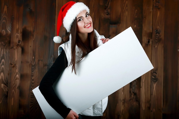 Ragazza della Santa che tiene il tabellone per le affissioni del segno dell'annata in bianco Donna di Natale in cappello della Santa che mostra carta