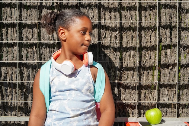 Ragazza della scuola afroamericana con lo zaino e le cuffie all'ingresso della scuola