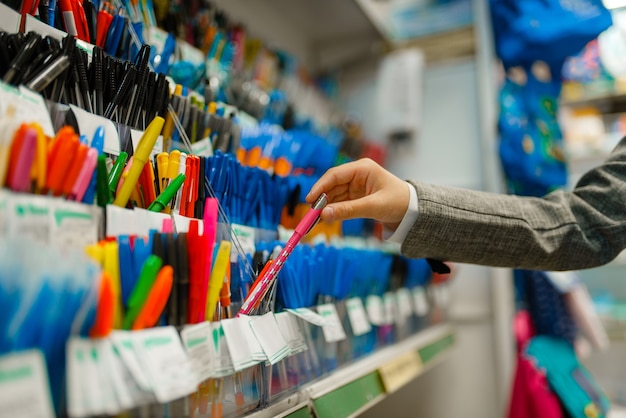 Ragazza della scuola che sceglie una penna sullo scaffale in cartoleria