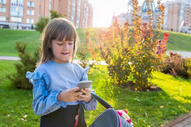 Ragazza della scuola con un telefono in mano all'aperto in una giornata di sole Bambino della scuola primaria