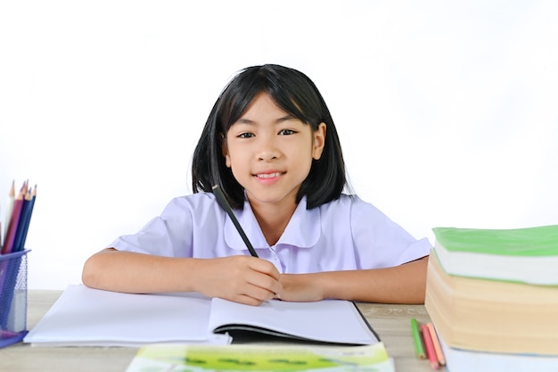 Ragazza della scuola in un'uniforme che si siede sul banco di scuola sul concetto di muro bianco imparando dall'insegnante.