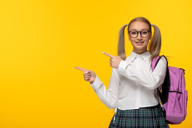 Ragazza della scuola sveglia felice della giornata mondiale del libro in uniforme con lo zaino rosa