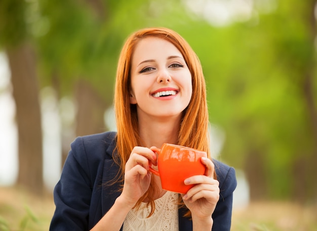 Ragazza della testarossa con la tazza arancio ad all&#39;aperto