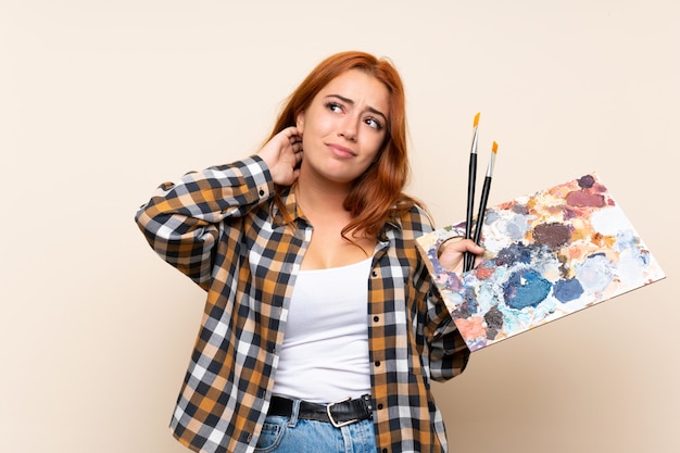 Ragazza della testarossa dell'adolescente che tiene una tavolozza sopra la parete isolata che pensa un'idea