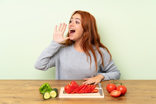 Ragazza della testarossa dell'adolescente con le verdure in una tabella che grida con la bocca spalancata