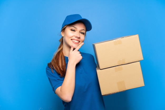 Ragazza delle consegne sopra il muro blu isolato felice e sorridente