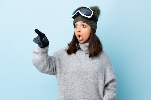 Ragazza dello sciatore della corsa mista con i vetri di snowboard sopra la parete blu che indica via