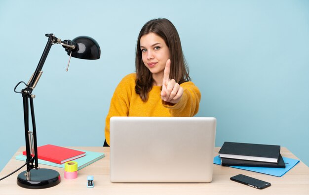 Ragazza dello studente che studia nella sua casa isolata sulla rappresentazione blu della parete e che solleva un dito