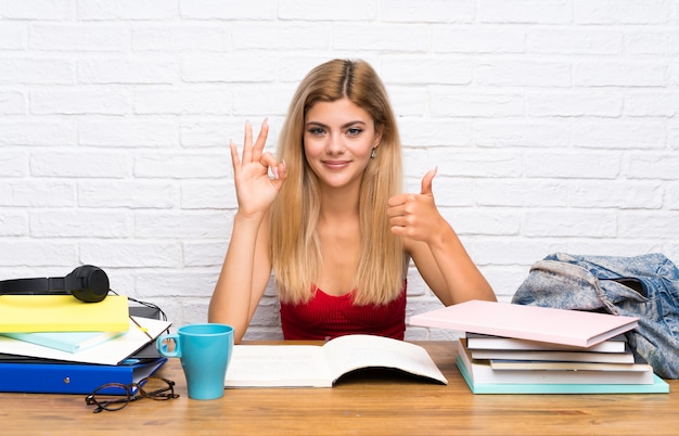 Ragazza dello studente dell&#39;adolescente all&#39;interno che mostra segno giusto e pollice sul gesto