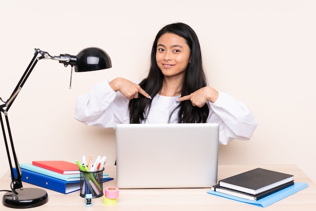 Ragazza dello studente in un posto di lavoro con un computer portatile isolato su beige con espressione facciale di sorpresa