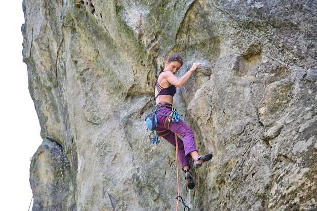 Ragazza determinata scalatore che si arrampica sulla ripida parete della montagna rocciosa Sportiva che supera il percorso difficile Impegnandosi in sport estremi e arrampicata su roccia concetto di hobby