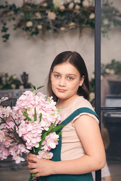 Ragazza di 12 anni in prendisole verde con fiori rosa in mano