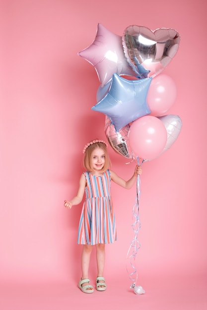 Ragazza di 5 anni in vestito con un mazzo di palloncini su una superficie rosa brillante