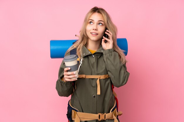 Ragazza di alpinista adolescente con un grande zaino sul muro rosa tenendo il caffè da portare via e un cellulare