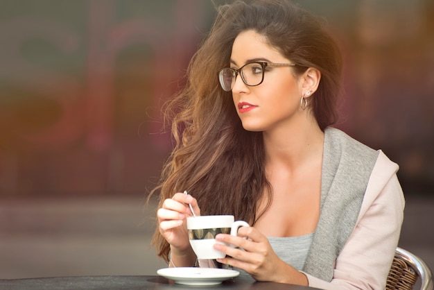 Ragazza di bellezza con i capelli lunghi e gli occhiali con una tazza di caffè