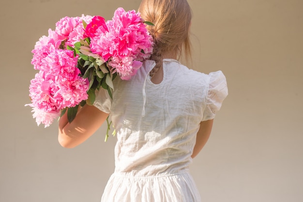 Ragazza di Boho che tiene peonie rosa nel cestino di paglia.