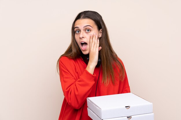 Ragazza di consegna della pizza che tiene una pizza sopra la parete isolata che bisbiglia qualcosa