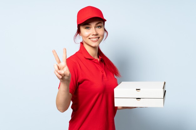 Ragazza di consegna della pizza che tiene una pizza sopra sorridere isolato e mostrare il segno di vittoria