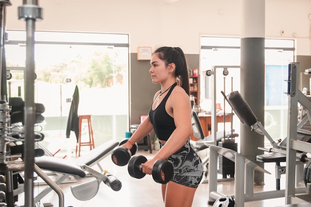 Ragazza di fitness che esegue esercizi per le spalle con i manubri in palestra