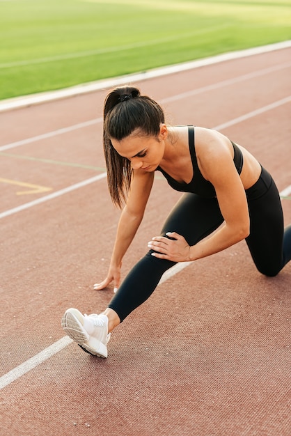 Ragazza di forma fisica che fa allenamento che si estende in uno stadio all'aperto