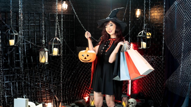 Ragazza di Halloween che indossa un costume da strega con un cappello che tiene una zucca lanterna e una borsa della spesa in tema di Halloween