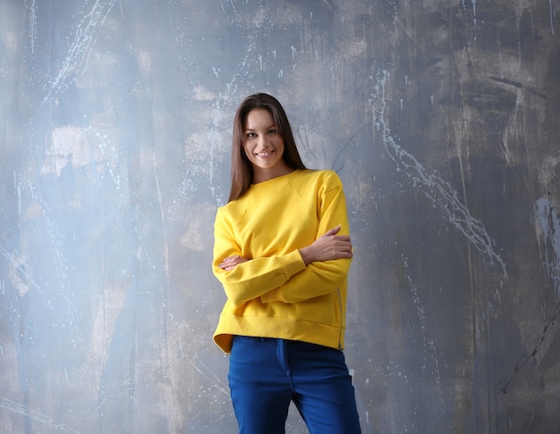 Ragazza di moda in maglione giallo su sfondo grigio muro