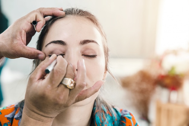 Ragazza di modello con truccatore che dipinge i suoi occhi con ombretto e l'eyeliner