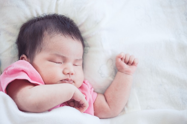 Ragazza di neonato asiatica che dorme sul letto bianco