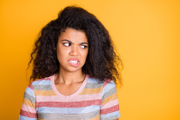 Ragazza di pelle scura dai capelli ondulati irritata che osserva da parte con disgusto