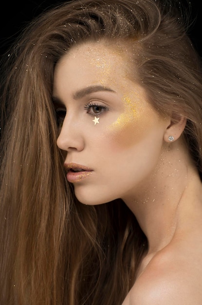 Ragazza di profilo con trucco glitter oro e stelle dorate per la festa di Capodanno su sfondo nero