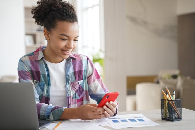 Ragazza di razza mista utilizza app mobili che tengono il telefono distratto dall'apprendimento sul laptop Dipendenza da gadget