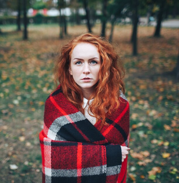 ragazza di redhead sul plaid rosso in autunno parco