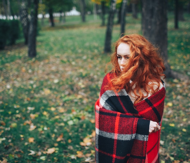 ragazza di redhead sul plaid rosso in autunno parco